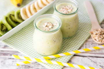Banana smoothie with kiwi and oats on a light wooden table. Healthy food