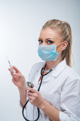 Attractive young blonde female doctor in blue mask with syringe and stethoscope