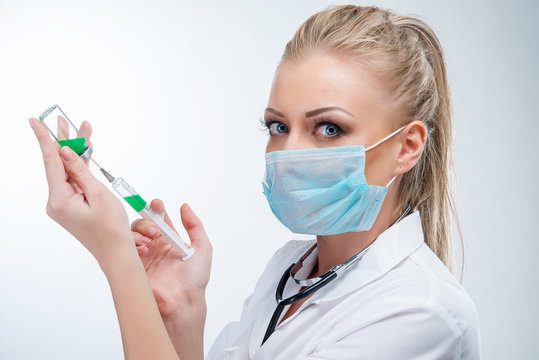 Attractive Young Blonde Female Doctor In Blue Mask With Syringe And Medicine