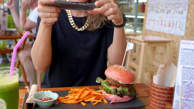 Trendy Woman Taking Photo of Burger with Smartphone in Cafe