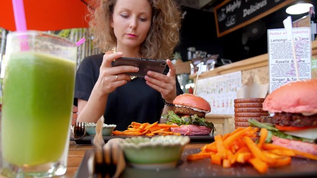 Woman Taking Picture of Veggie Burger with Mobile Phone in Healthy Cafe