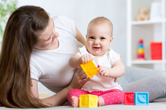Mother and baby girl playing with color developmental toys in nursery
