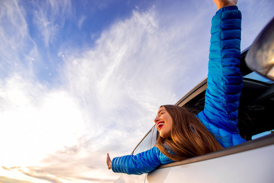 Young Woman In Blue Jacket Enjoying Beautiful Cloudscape Looking Out The Car Window With Raised Hands On The Sunrise