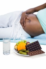 Obraz na płótnie Canvas Pregnant woman lying by fruits and chocolates