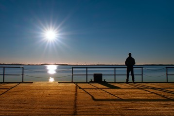 Fototapeta premium Man stand on wharf construction and looking at sea. Sunny clear blue sky, calm level