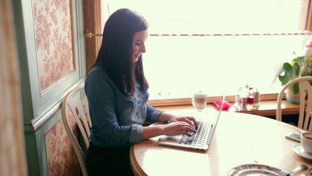 Beautiful happy young woman sitting in the cafe working on the laptop