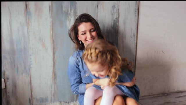 Beautiful happy family mother and daughter playing on the carpit tickle baby play with the baby smiling laughing vintage wood background same denim dresses