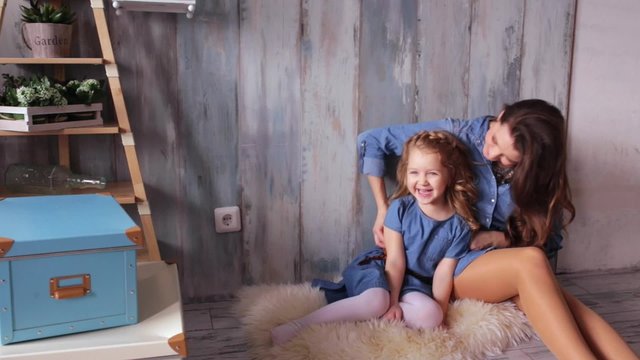 Beautiful happy family mother and daughter playing on the carpit tickle baby play with the baby smiling laughing vintage wood background same denim dresses