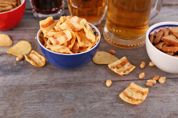 Mugs of beer and bowls with snacks on wooden table