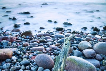 Romantic atmosphere in peaceful morning at sea. Big boulders sticking out from smooth wavy sea. Pink horizon