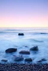 Romantic morning at sea. Big boulders sticking out from smooth wavy sea. Long exposure