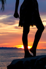 Silhouette of a dancing girl on a rock by the sea on a background of tropical sunset
