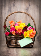 Fototapeta na wymiar Roses in the basket and a greeting card on wooden background