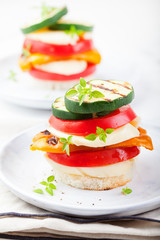 Grilled vegetables and cheese gratin stacked on a plate with fresh basil on white background