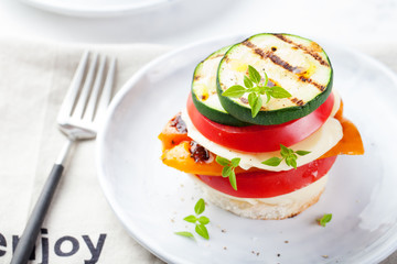 Grilled vegetables and cheese gratin stacked on a plate with fresh basil on white background