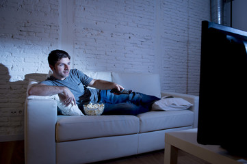 young attractive man at home lying on couch at living room watching tv holding remote control