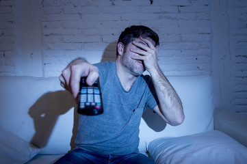 man holding tv remote control sitting at living room couch watching television blocking his eyes