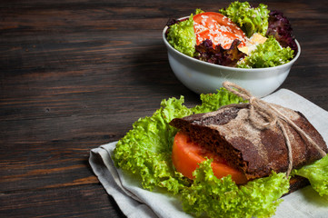Sandwich on the wooden table with slices of fresh tomatoes, ham, cheese and lettuce