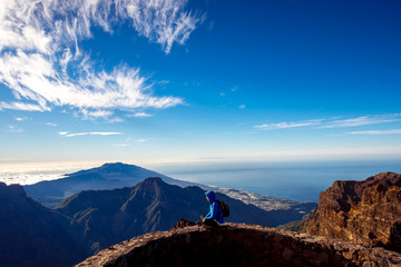 Woman in blue jacket and backpack traveling mountains near Andenes viewpoint on La Palma's island highest point in Spain