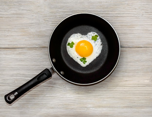fried eggs in heart shape in the pan on the wooden bachground