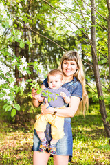 Happy young woman and little son in the blooming spring garden. Mothers day holiday concept