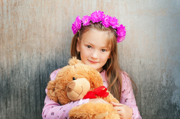 Close up portrait of adorable little girl with bright pink flower headband, holding teddy bear