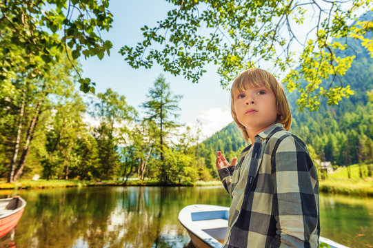 Cute little boy hiking in swiss Alps, resting by the lake