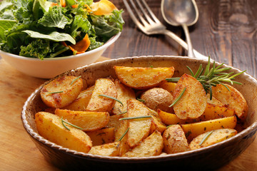 Roasted potato in brown bowl with fresh salad on wooden table