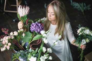 Florist at work: pretty young blond woman making fashion modern bouquet of different flowers