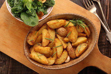 Roasted potato in brown bowl with fresh salad on wooden table