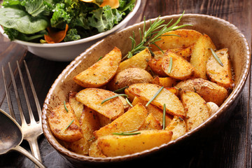 Roasted potato in brown bowl with fresh salad on wooden table