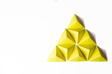 Yellow origami pyramid with tetrahedrons with copy space on the left side.