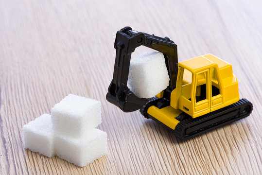 Small, yellow toy excavator grabbing a piece of sugar