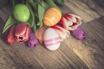 Photograph of a couple of colorful easter eggs with a bunch of tulips on wooden surface