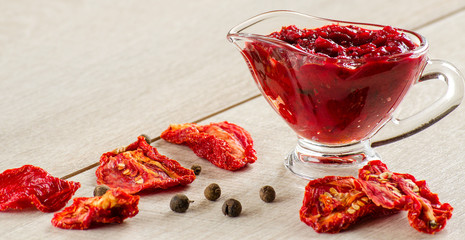 The tomato sauce in the saucepan, sun-dried tomatoes on wooden t