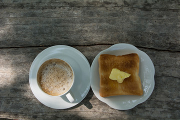a cup of coffee with bread and butter on top on wood background