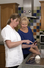 A carer using a mobile phone and working with a client in the client's kitchen
