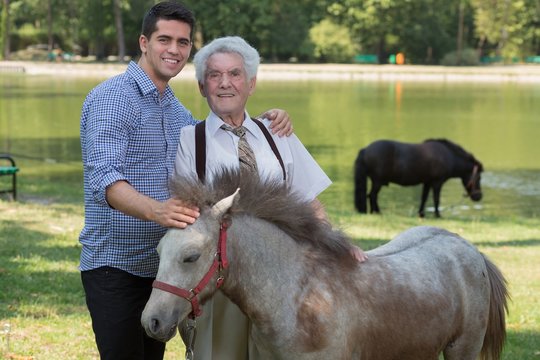 Grandfather and grandchild stroking pony