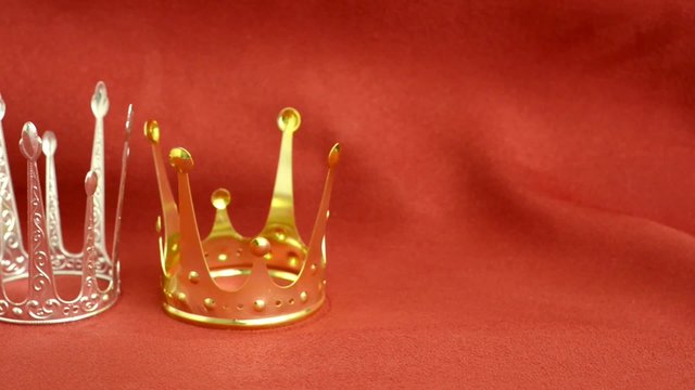Gold abd silver crowns on red velvet background. Slow sliding motion. Symbol of success, luxury and history.