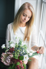 Obraz na płótnie Canvas Florist at work: pretty young blond woman holds fashion modern bouquet of different flowers