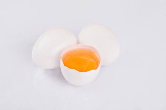Whole and broken raw white eggs on white background