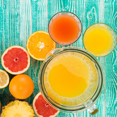 fresh juice from citrus fruits - lemon, grapefruit, orange, pine apple  in blender bowl and glasses on  turquoise colored wooden background, top view. copy space, free space for your text. - 104312307