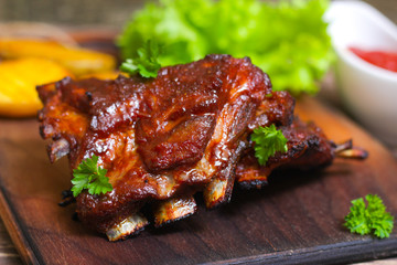 Delicious barbecued lamb ribs seasoned with a spicy basting sauce and served with chopped fresh herbs and potatoes on an old rustic wooden chopping board in a country kitchen