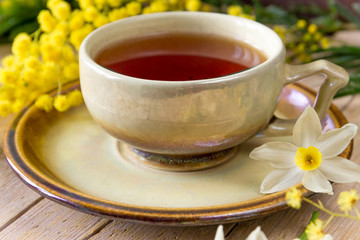 Чашка чая украшенная веточками мимозы и нарциссами