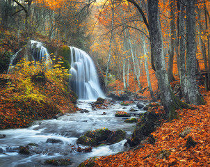 Beautiful waterfall at mountain river in colorful autumn forest with red and orange leaves at sunset. Nature landscape