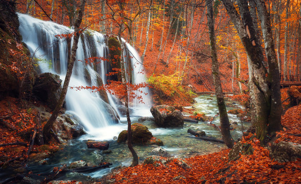 Fototapeta Beautiful waterfall at mountain river in colorful autumn forest with red and orange leaves at sunset. Nature landscape