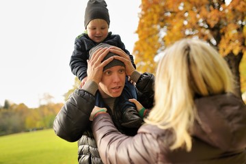 Wife corrects clothes for husband with child on a shoulders in park