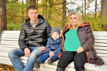Family sits in autumn park on bench