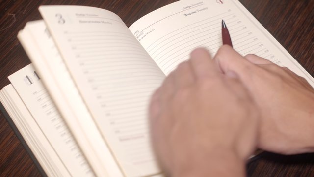 Right man's hand open paper leather notebook and write number phone by a pen