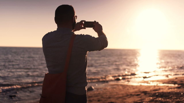 Man taking photo of sunset standing on beach 
